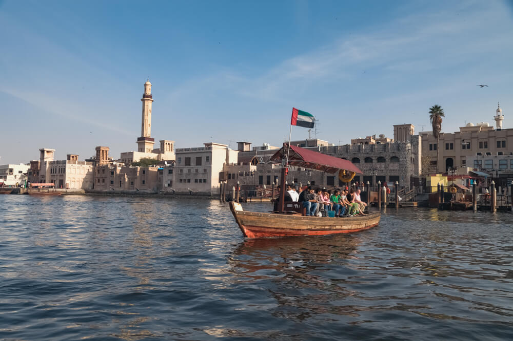 Abra boat on Dubai Creek with traditional buildings in the background.