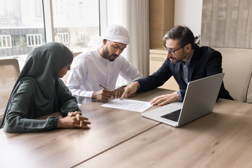 Business meeting with two men and a woman signing documents at a table.