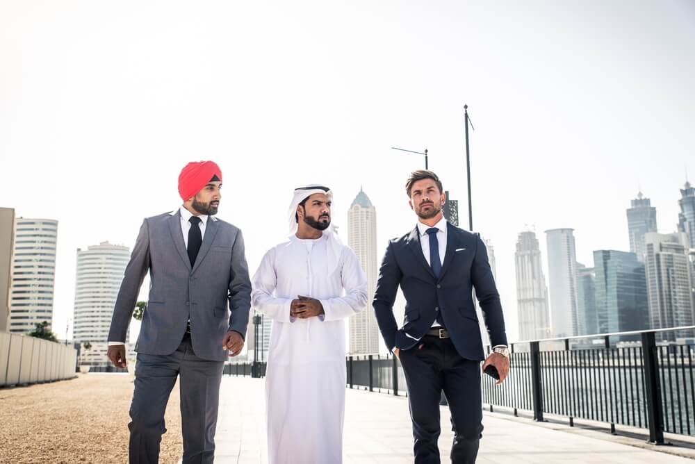 Three businesspeople walking together in Dubai wearing formal attire.