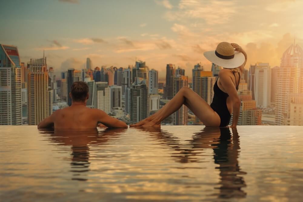 Couple relaxing at an infinity pool with a city skyline at sunset.