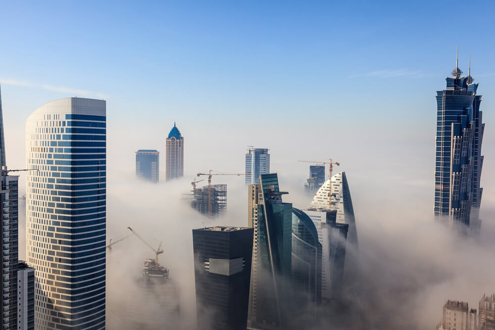 Dubai skyline with skyscrapers emerging through thick morning fog.