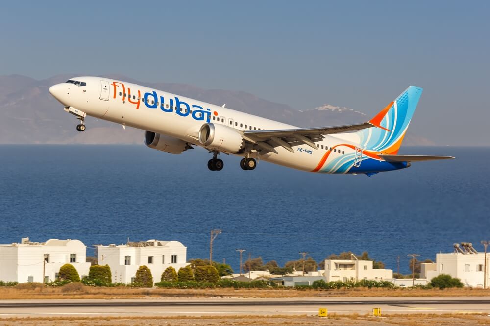 Flydubai airplane taking off with a scenic view of the sea and mountains.