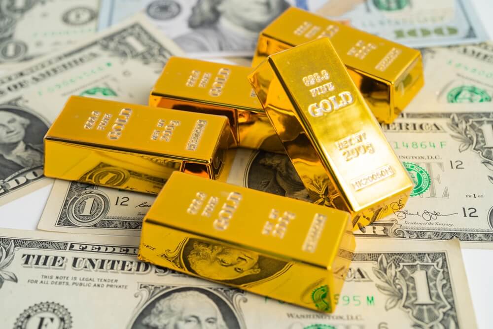 Gold bars stacked on top of US dollar bills, representing wealth and investment.