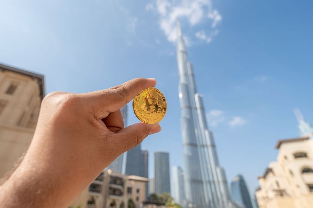 Hand holding a Bitcoin coin with the Burj Khalifa in the background.