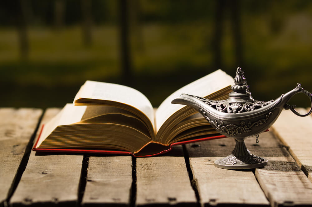 Open book next to a decorative magic lamp on a wooden table.