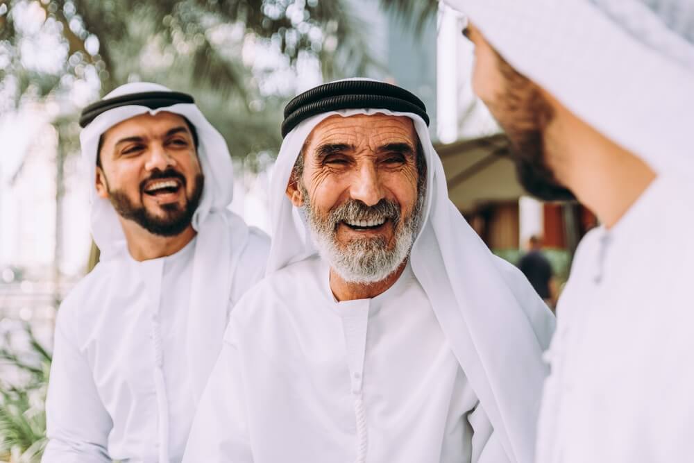 Smiling men in traditional dress enjoying conversation outdoors.