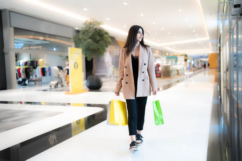 Woman walking through a shopping mall carrying colorful shopping bags.